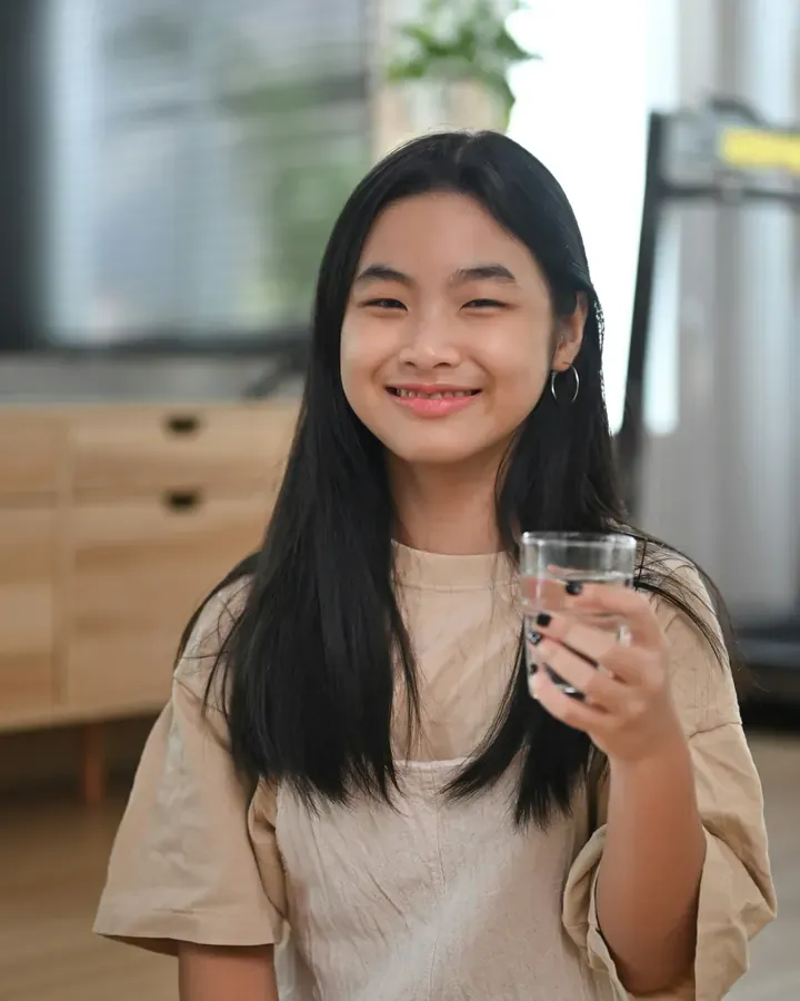 A teen girl at home in the morning, smiling, with a glass of water